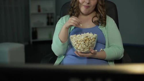 Joven gordita riendo, comentando en el programa de televisión y comiendo palomitas de maíz desordenadamente
