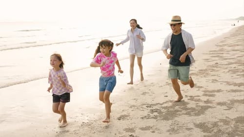 4K Asiatische Familieneltern mit zwei kleinen Töchtern spielen gemeinsam am Strand bei Sonnenuntergang.