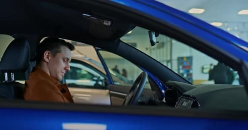 Man Sits in Blue Car at Dealership