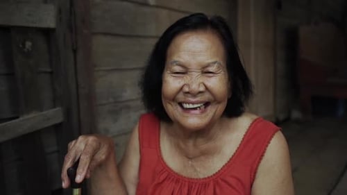 slow-motion of Thai elderly woman in round-necked sleeveless collar laughing in old wooden home