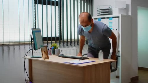 Man Uses Hand Sanitizer at Office Desk