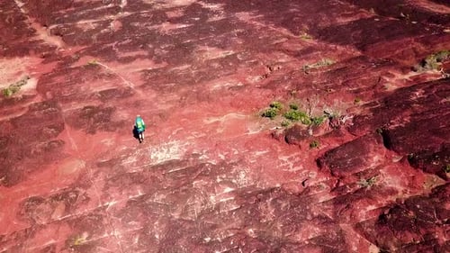 Drone footage of a girl with a hiking pack facing away from camera, hiking along magnificent red roc
