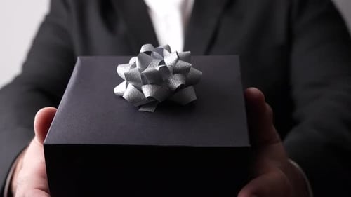 Person Presenting Black Gift Box with Silver Bow