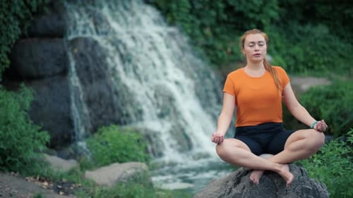 Redhead Woman Meditating by a Tranquil Waterfall