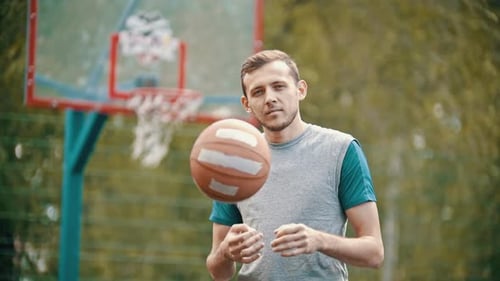 Ein Mann steht auf einem Sportplatz und wirft den Basketballball hoch