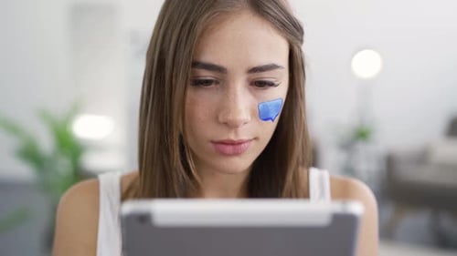 Close-up Portrait of Young Cute Woman Sitting at Home, Looking in the Tablet and Smiling