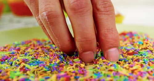 Hand Decorating Cupcake with Multicolored Sprinkles