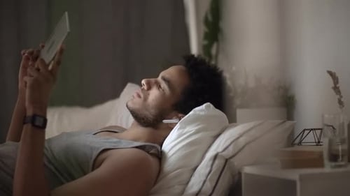 Man Relaxing in Bed, Using Tablet Device