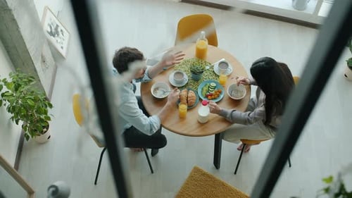 Top View of Young Husband and Wife Eating Food for Breakfast and Talking in Kitchen in Apartment
