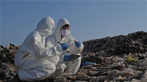 Two Scientists Examine Trash in Protective Gear