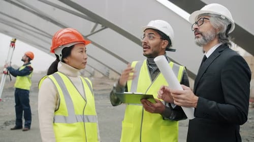 Group of Workers Talking to Construction Inspector Looking at Blueprints in Building Area