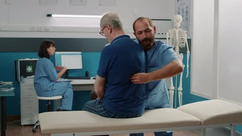 Therapist Palpates Senior Man's Back in Office