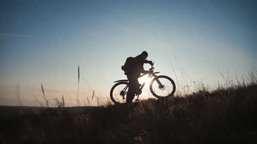 Die Silhouette des Mountainbike-Fahrers auf dem Hügel mit Fahrrad bei Sonnenuntergang. Sport, Reisen und