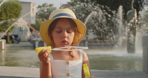 Cute Little Girl Blows Soap Bubbles on the Background of a Fountain