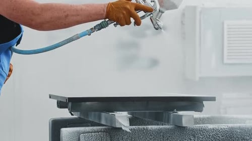 Der Arbeiter bedeckt die flache Oberfläche des Details mit einer weißen Sprühfarbe