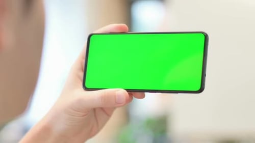 Young Man Looking at Smartphone with Green Chroma Screen