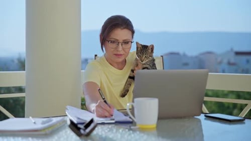 Home Arbeitsplatz Freiberuflerin arbeitet remote mit Haustierkatze im Arm