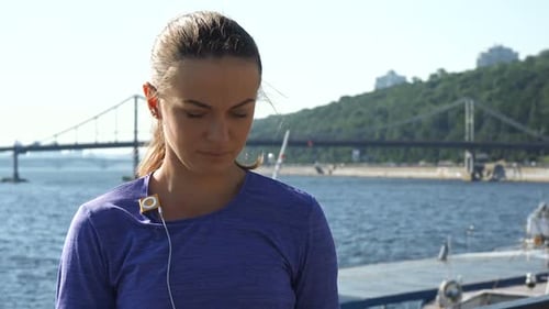 Woman Puts in Earbuds before Workout by River
