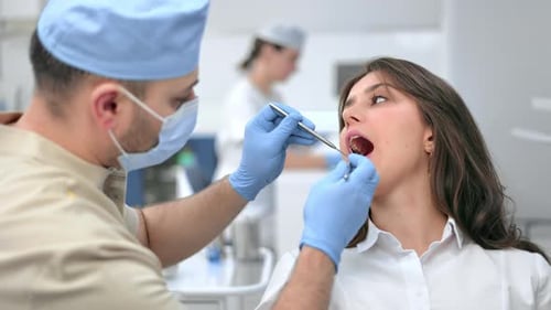 Männlicher Zahnarzt untersucht Zähne einer Patientin und verwendet zahnmedizinische Geräte