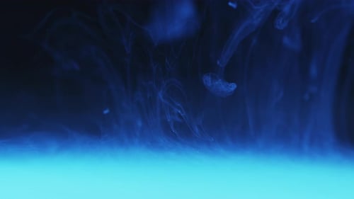 Encre blanche en suspension dans l'eau sur fond de fumée de teinte bleu clair