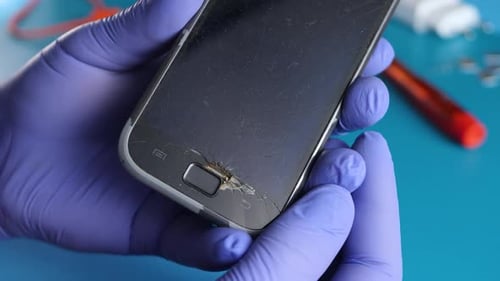 Una mano irreconocible sostiene un teléfono inteligente con pantalla táctil rota