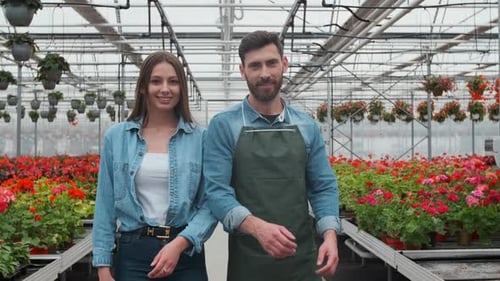 Smiling Man and Woman in Flower-Filled Greenhouse
