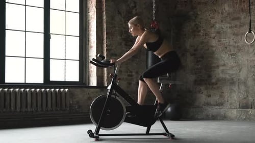 The woman in sport clothes is working out on the exercise bike in the green gym.