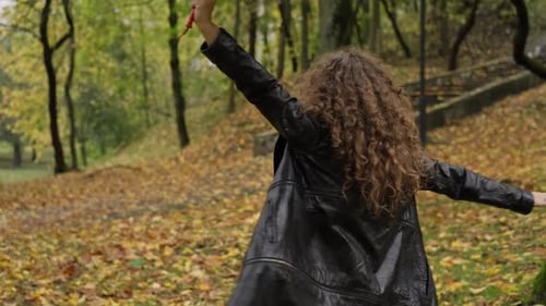 Positive Frau dreht sich mit Regenschirm aus Blättern im Herbstpark