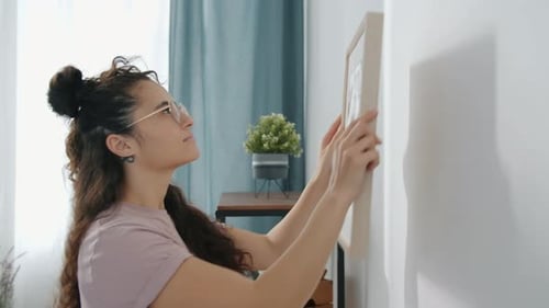 Woman Hanging Picture on Wall in Bright Room