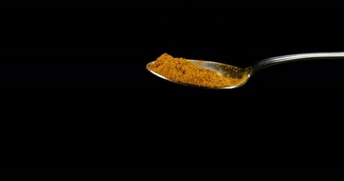 Spoon and Curry Powder falling against Black Background, Slow motion 4K