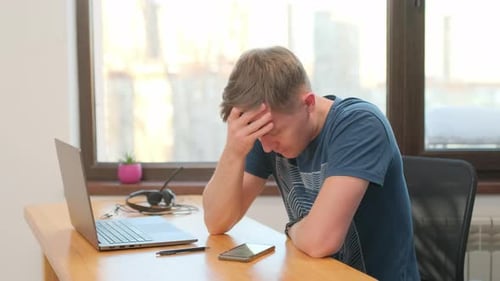 young business man indoors at home using laptop computer and mobile phone