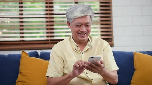 Senior Man Smiling Using Smartphone in Living Room