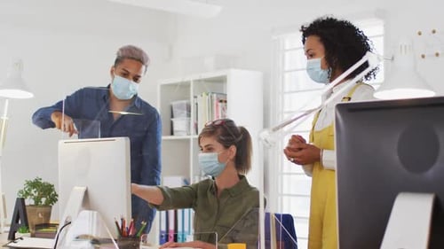 Office colleagues wearing face masks discussing over computer at office
