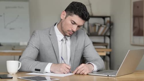 Man Writing at Desk in Office Environment