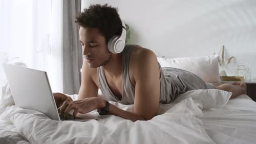 Man with Headphones Lies in Bed Typing