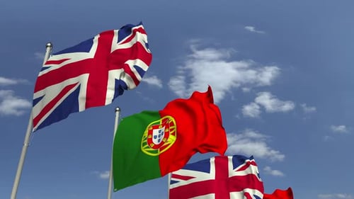 Waving Flags of Portugal and United Kingdom Against Blue Sky