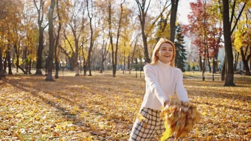Cute Young Woman Swirling with Autumn Leaves Throwing Them in Air and Dancing in Autumn Park Slow