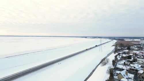 Power Lines with Towers Near Road with Traffic and Village in Winter