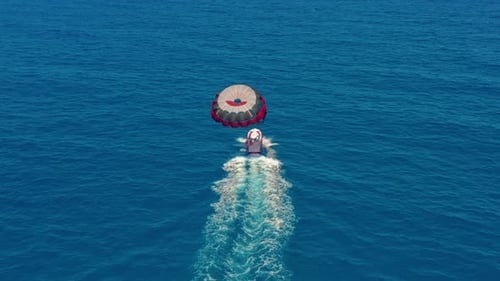Aerial View. People Flying on a Colorful Parachute Towed By a Motor Boat. Parasailing in Blue Sky.
