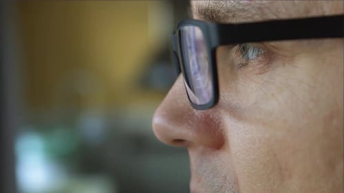 Man wearing glasses looks at computer screen close up