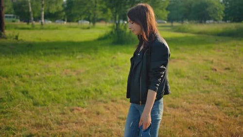 A Young Female in Jeans Leading Her Dog for a Walk in the Park on a Leash.
