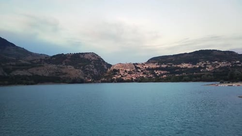 Aerial Panning Shot of Trees at Lakeshore Near Mountain Range Drone Flying Forward Over Lake Against
