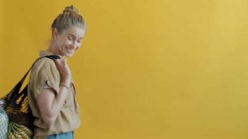 Cámara lenta de una niña feliz que lleva una bolsa reutilizable con comida sobre fondo amarillo