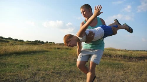 Father Twirling Son Around in Grassy Field