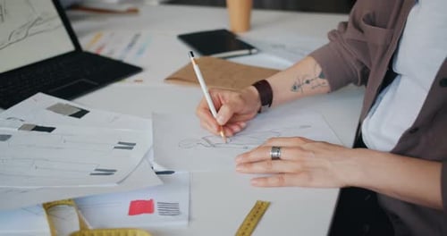 Close-up of Female Designer's Hand Drawing Sketches of Clothes on Paper on Table