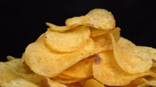 Craft crispy potato chips rotating on black background close up. Golden fried potatoes in macro