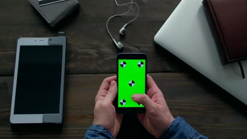 Hands of Man Using Smartphone with Green Screen on Wood Table