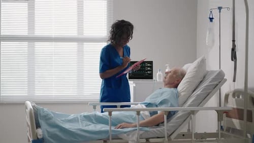 An Elderly White Man of 6070 Years Old is Lying in a Hospital Bed Talking to a Black Woman Doctor