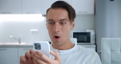 Excited man looks at phone in modern kitchen