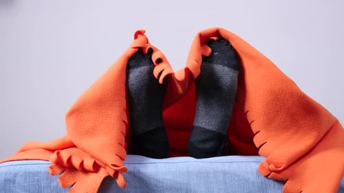 Legs in Socks Resting Under Orange Blanket